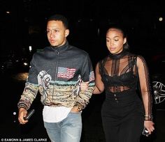 a man and woman walking down the street at night with an american flag sweater on