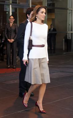 a woman walking down the street in high heels and a white top with long sleeves