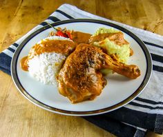 a white plate topped with meat and rice on top of a wooden table next to a napkin