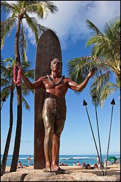 a man standing next to a surfboard on top of a sandy beach