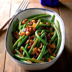 a bowl filled with green beans and bacon on top of a wooden table next to a fork