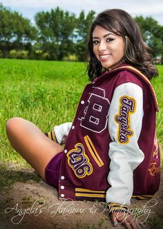 a woman sitting on the ground wearing a maroon and white varsity jacket with gold lettering