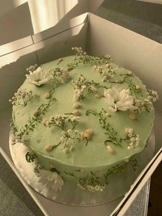 a green cake with white flowers in a box