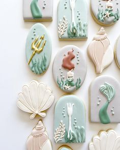 decorated cookies arranged in the shape of mermaids and seashells on a white surface