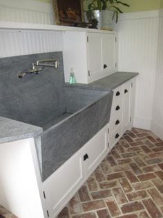 a kitchen with white cabinets and grey counter tops, an apron style sink in the center