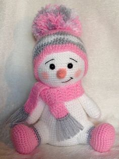 a crocheted snowman with a pink hat and scarf sitting on a white blanket