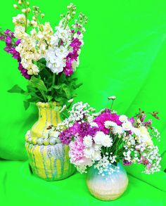 two vases with flowers are sitting on a green cloth covered surface, one has purple and white flowers in it