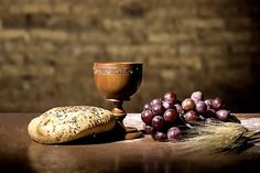 a table topped with bread and grapes next to a chalicette on top of a wooden table