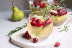 two glasses filled with drinks and garnished with cranberries on a cutting board