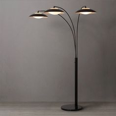 a lamp with three lights on it in front of a gray wall and wooden floor