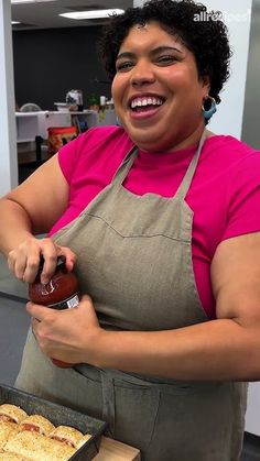 a woman in an apron is holding a bottle and spreading ketchup on food