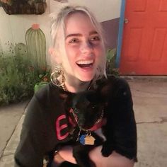 a woman with white hair holding a black cat in her arms and smiling at the camera