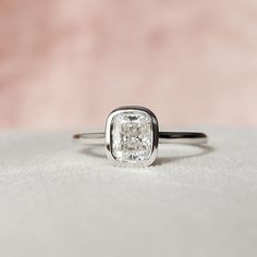 an engagement ring with a square cut diamond in the center, sitting on a white surface