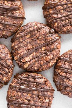 chocolate covered cookies with nuts and drizzled in chocolate on a white surface