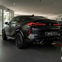 the rear end of a black bmw suv in a showroom with two other cars