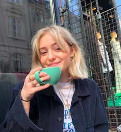 a woman holding a green coffee cup in her right hand and looking at the camera