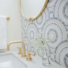 a vase with flowers in it sitting next to a bathroom sink under a large mirror