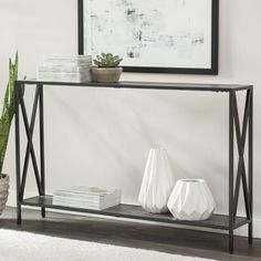 a black metal console table with two white vases on it and a plant next to it