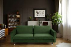 a green couch sitting on top of a wooden floor next to a potted plant