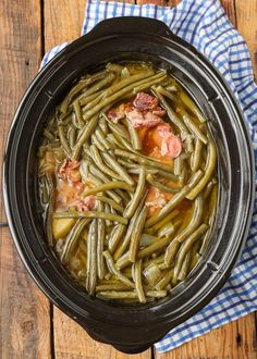 a crock pot filled with green beans and meat on top of a wooden table