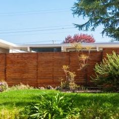 a wooden fence in front of a house with green grass and bushes around the perimeter