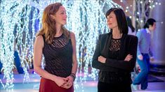 two women standing next to each other in front of some lights and trees at night