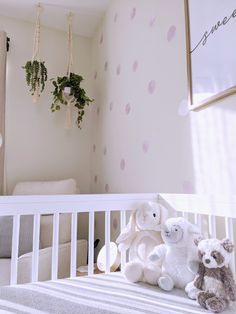 two stuffed animals sitting on top of a crib next to a wall with polka dot decals