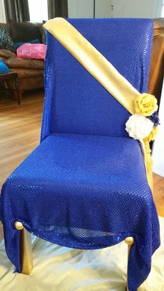 a blue chair with a gold sash and flower on it's back, sitting in a living room