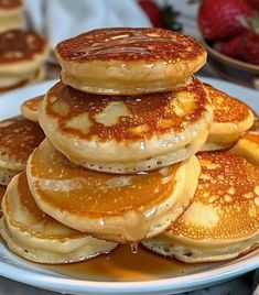 pancakes stacked on top of each other on a white plate with syrup and strawberries in the background