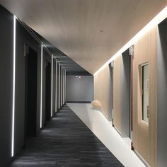 an empty hallway with several doors and lights on either side of the corridor is lit by recessed lighting