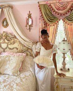 a woman in a white dress standing next to a bed with pink walls and curtains