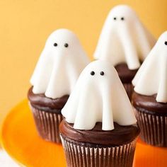 chocolate cupcakes decorated with white frosting and ghost faces on an orange plate