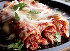 a black plate topped with lasagna covered in sauce and cheese garnished with cilantro