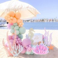 an umbrella and decorations on the beach for a mermaid themed birthday party or baby shower