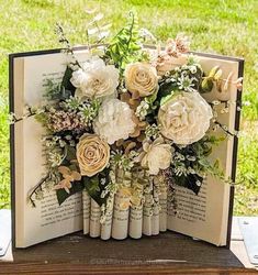 an open book with flowers on it sitting on top of a wooden table in the grass