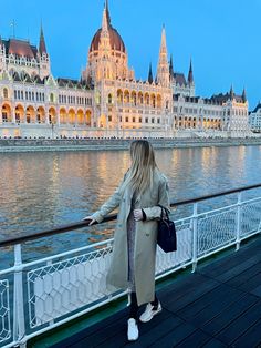 a woman standing on the edge of a bridge looking at buildings in front of water