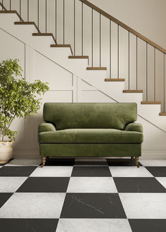 a green couch sitting in front of a black and white checkered floor next to a stair case