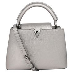 Louis Vuitton Capucines BB Metallic Grey Top Handle Handbag. This beautiful shoulder bag is composed of luxurious textured Taurilloun leather in metallic grey. The handbag features a single rolled leather reinforced top handle with stylized links and an adjustable and detachable crossbody strap. Crossover flap that inserts behind the prominent LV, and opens to a partitioned leather interior with an interior zip pocket. Silver toned metal hardware. 4 protective metal bottom studs. Measurements: L High-end Silver Shoulder Bag With Palladium Hardware, High-end Silver Bag With Palladium Hardware, Luxury Silver Crossbody Shoulder Bag, High-end Silver Top Handle Shoulder Bag, High-end Silver Shoulder Bag With Silver-tone Hardware, High-end Silver Bags With Silver-tone Hardware, High-end Silver Top Handle Bag, High-end Silver Bag With Silver-tone Hardware, Designer Silver Top Handle Shoulder Bag