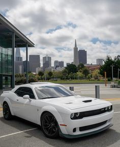 a white sports car parked in front of a building with the city skyline behind it