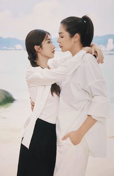 two women standing next to each other near the ocean