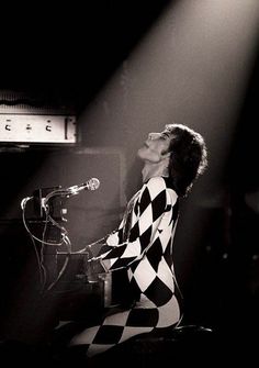 a woman in checkered dress sitting at a microphone and singing into a mic on stage