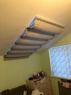 a room with a bed, dresser and window covered in white fabric on the ceiling