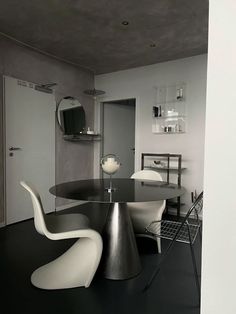 a black and white photo of a modern dining room with chairs, table and mirror