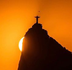 the sun is setting behind a statue on top of a hill with a cross at the top