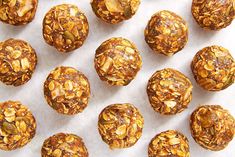 several balls of granola are lined up on a sheet of parchment paper with nuts in the middle