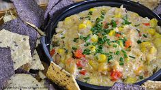 a black bowl filled with corn and vegetable dip surrounded by tortilla chips on the side