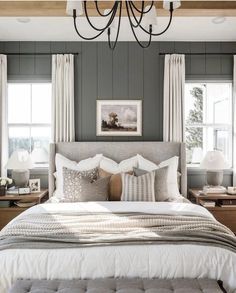 a large bed sitting under a chandelier next to two windows in a bedroom