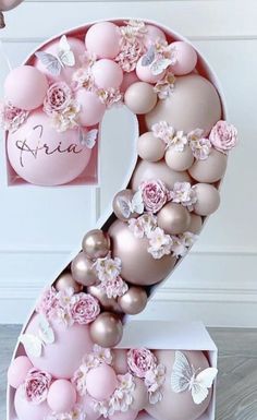 the number two made out of balloons and pink flowers is displayed in front of a white wall