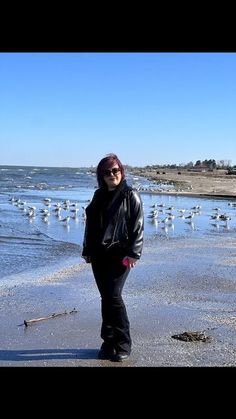 a woman standing on top of a sandy beach next to the ocean with seagulls in the background