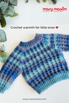 a blue and white sweater sitting on top of a table next to green leaves with the words crochet warm for little ones